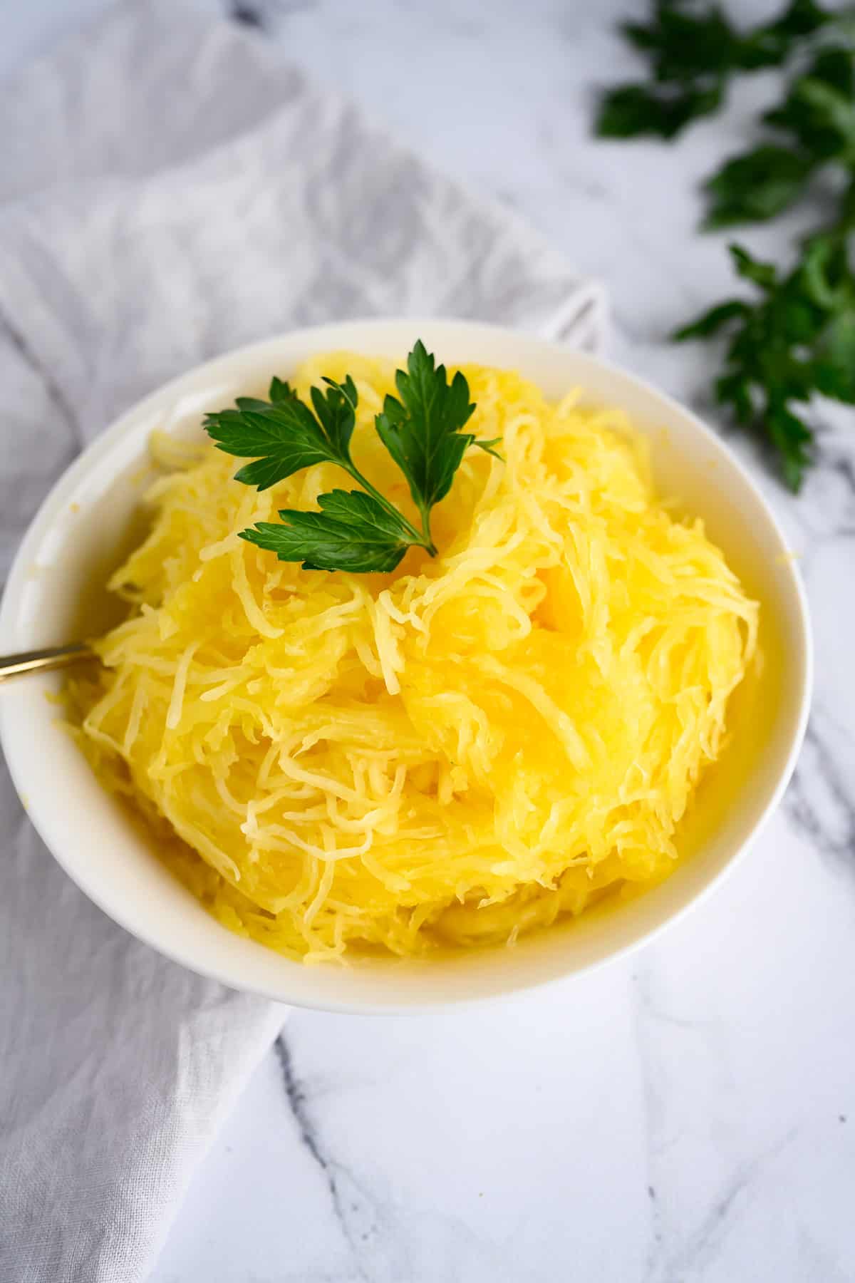 Cooked Spaghetti Squash "noodles' in a white bowl, garnished with a sprig of parsley