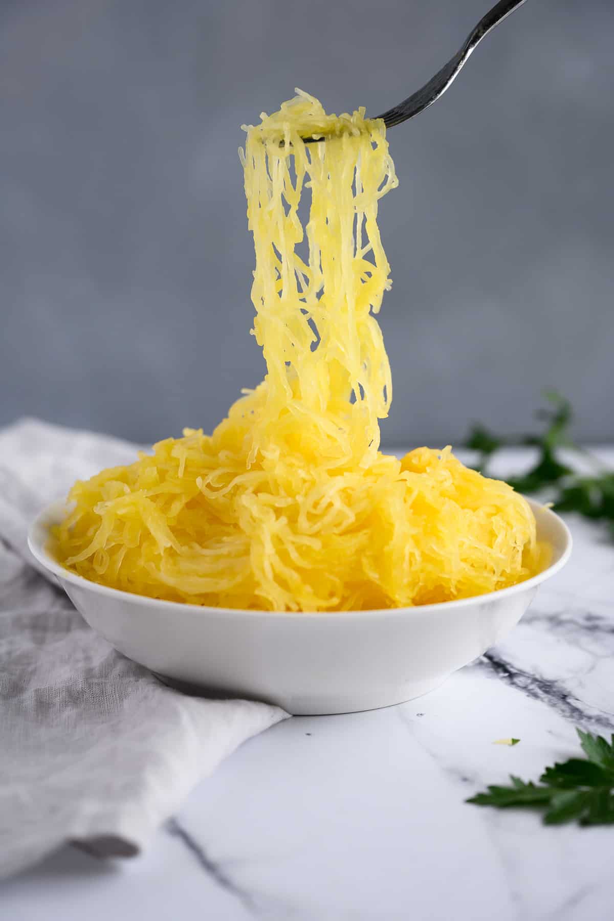 fork holding long strands of spaghetti squash over a bowl full of spaghetti squash.