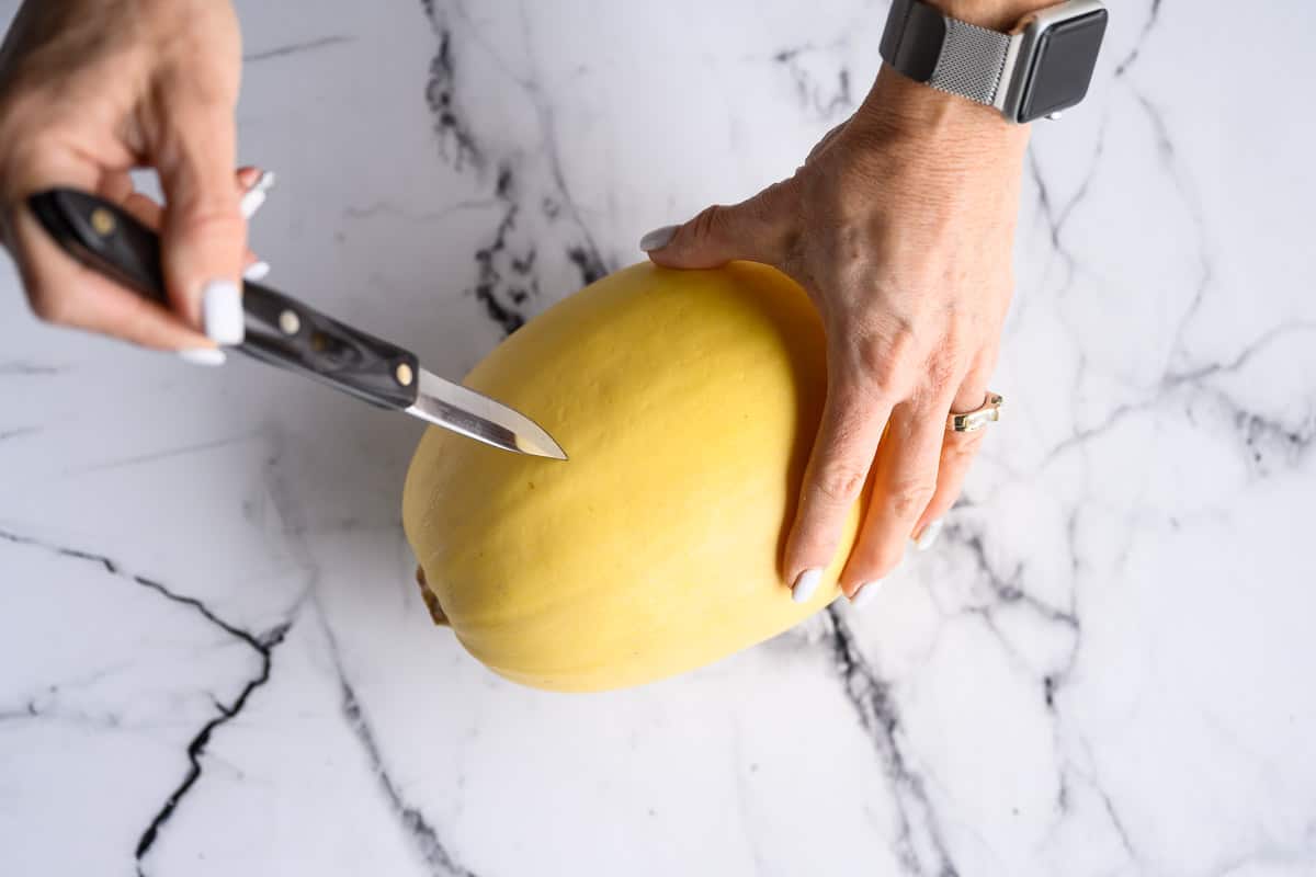 whole raw spaghetti squash being pierced by a pairing knife.