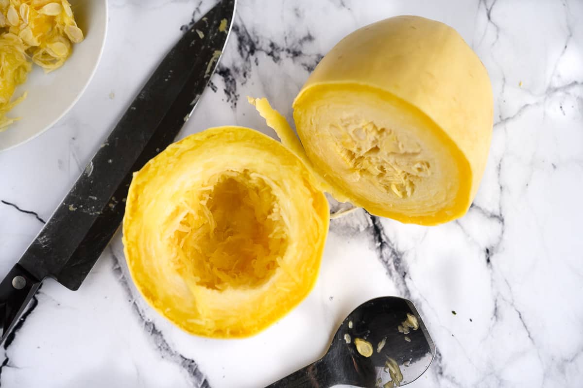 cooked whole spaghetti squash cut in two, one half has seeds removed.