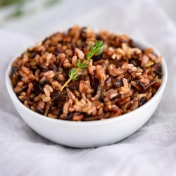 white bowl of cooked wild rice garnished with a sprig of thyme