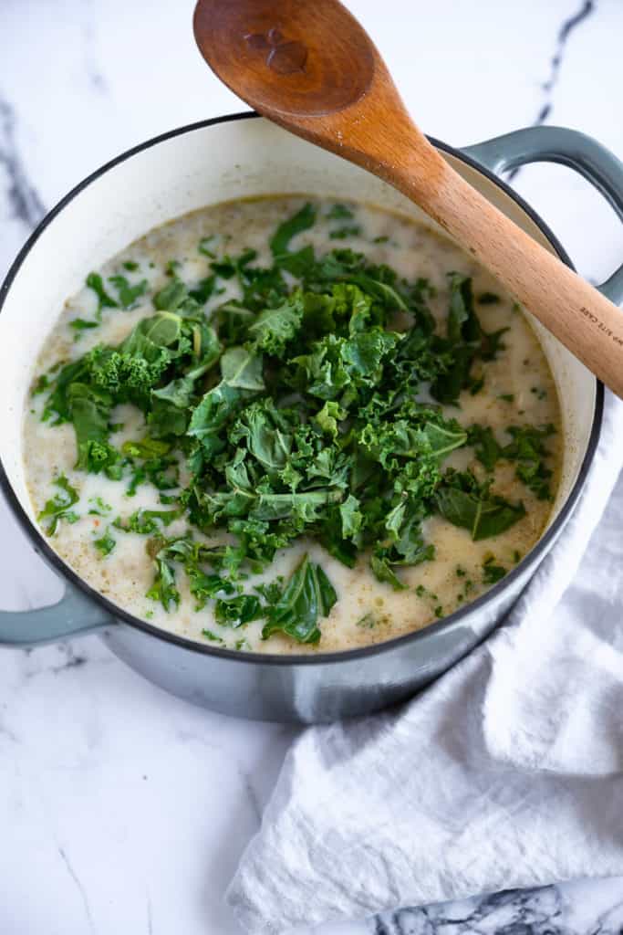 dutch oven full of creamy sausage soup with a pile of kale leaves on top