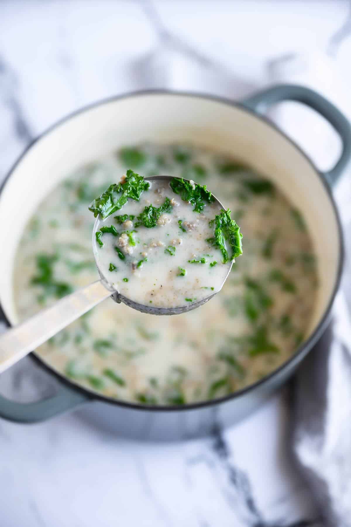 ladle of sausage and kale soup over a dutch oven.