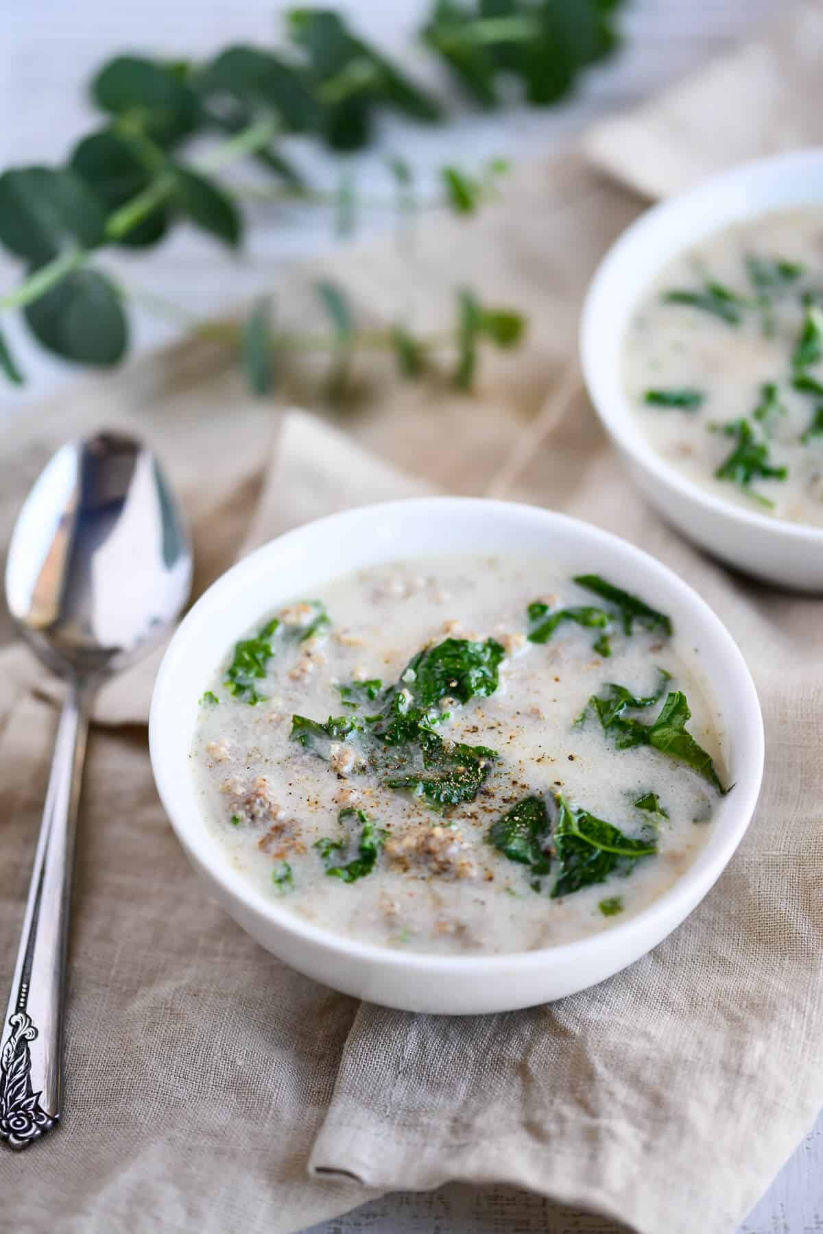 two bowls of sausage and kale soup garnished with pepper