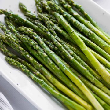 platter of asparagus garnished with oil and lemon