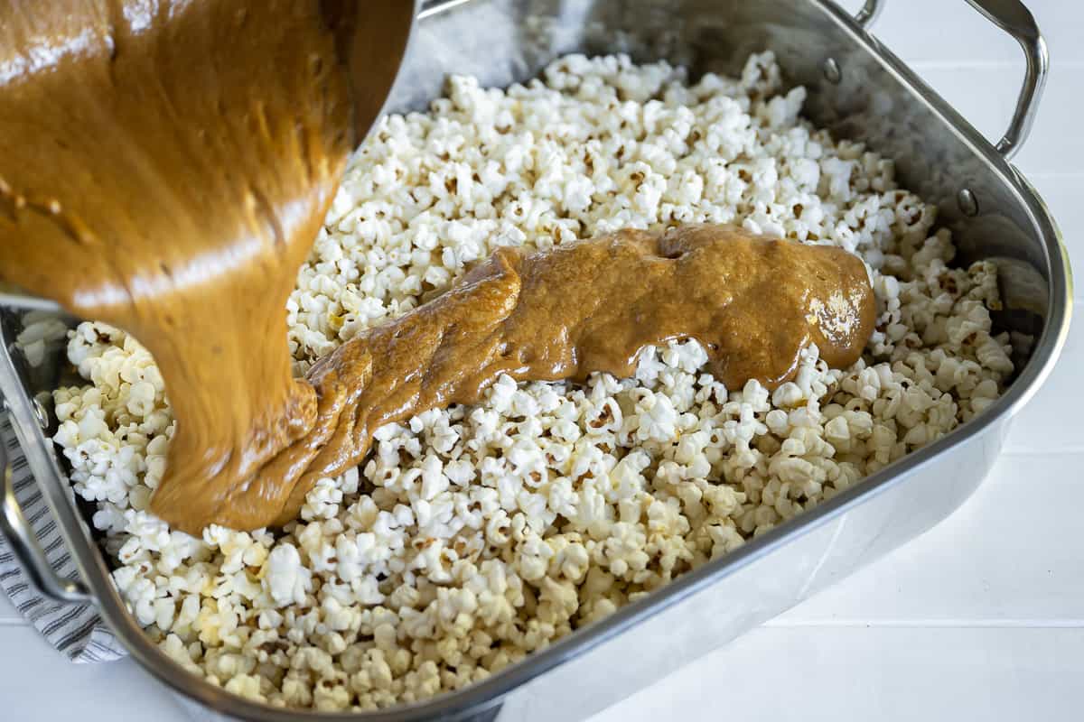 caramel sauce being poured over popcorn in a roasting pan