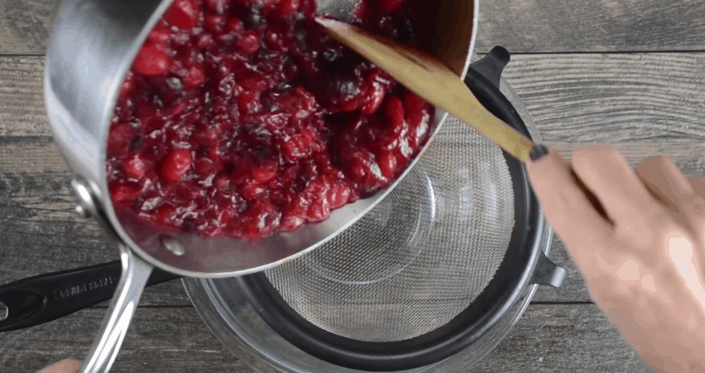 pan of whole cooked cranberries being poured into a fine mesh sieve