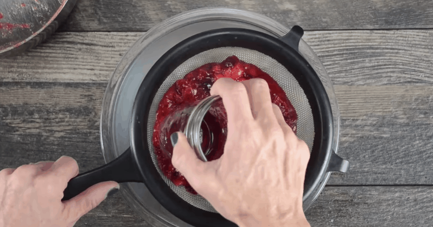 straining homemade cranberry sauce with a fine mesh sieve and a mason jar