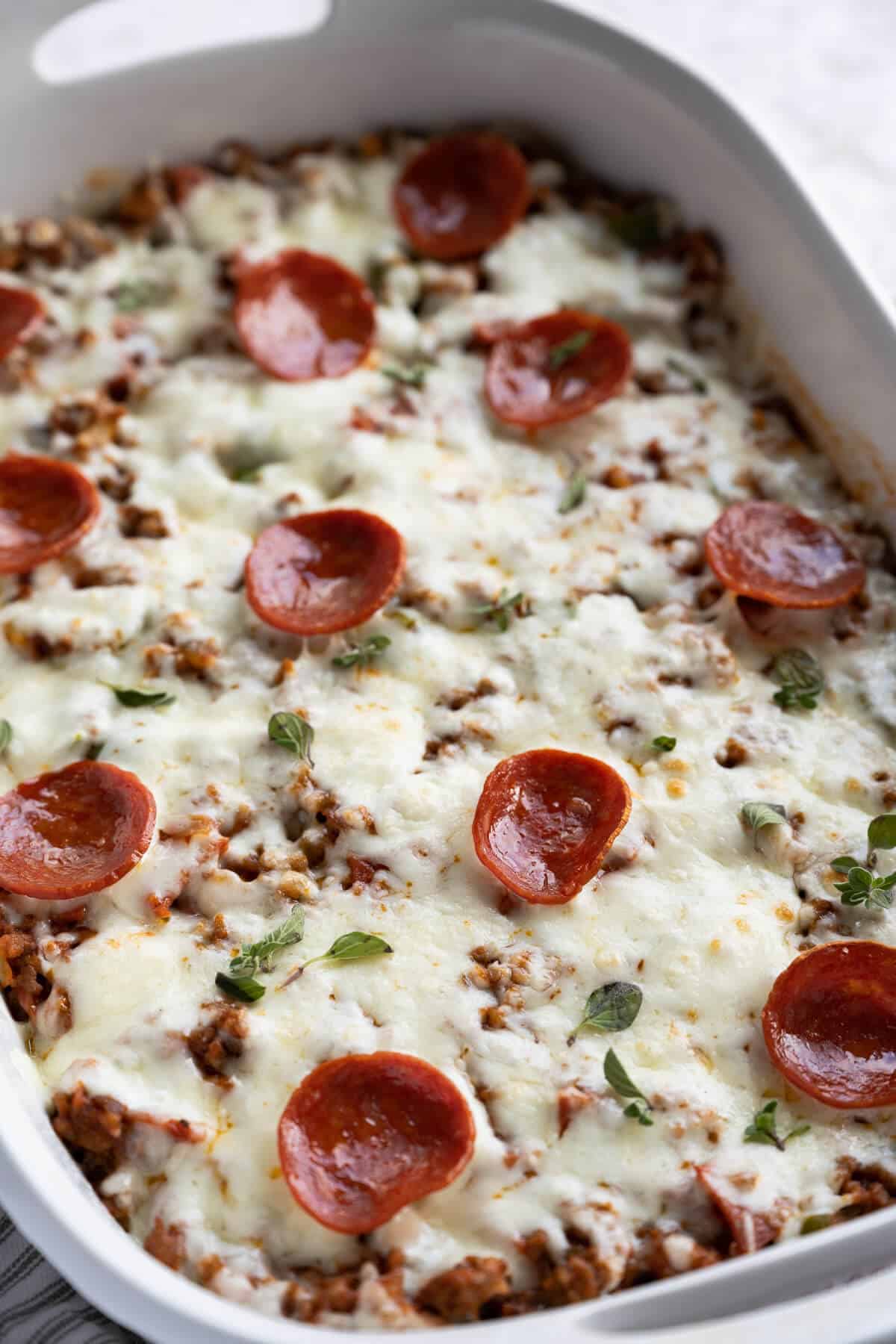 Keto Pizza Casserole in a white casserole dish garnished with fresh oregano