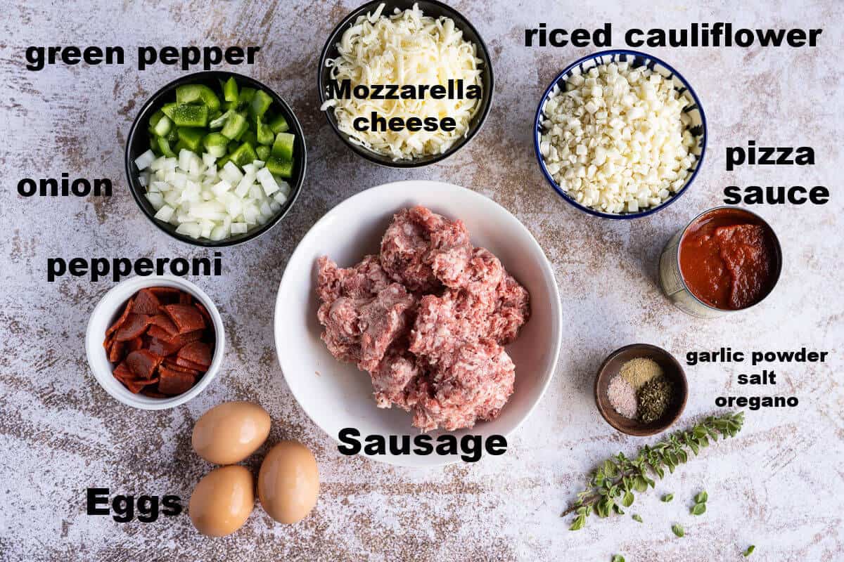 ingredients for keto pizza casserole, sausage, pepper, onion, pepperoni, cheese, eggs, pizza sauce riced cauliflower, and seasonings