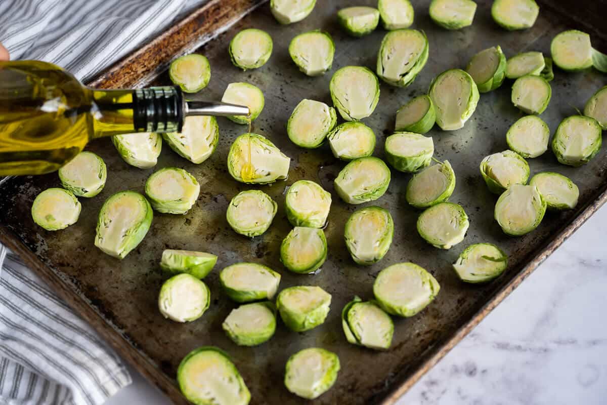 olive oil being poured over sliced brussels sprouts