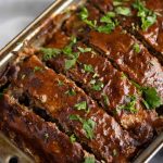 sliced low carb meatloaf in a loaf pan that has been glazed with sauce and garnished with parsley