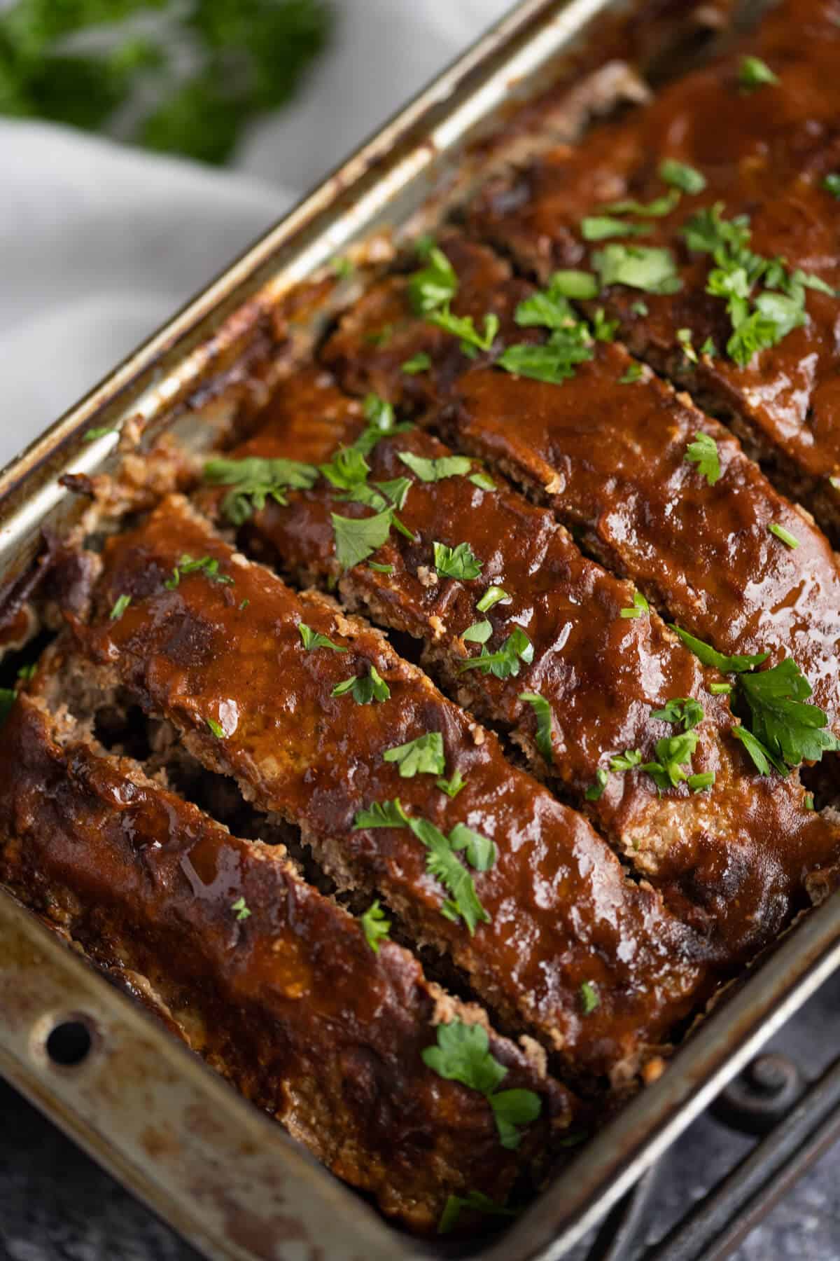 sliced low carb meatloaf in a loaf pan that has been glazed with sauce and garnished with parsley
