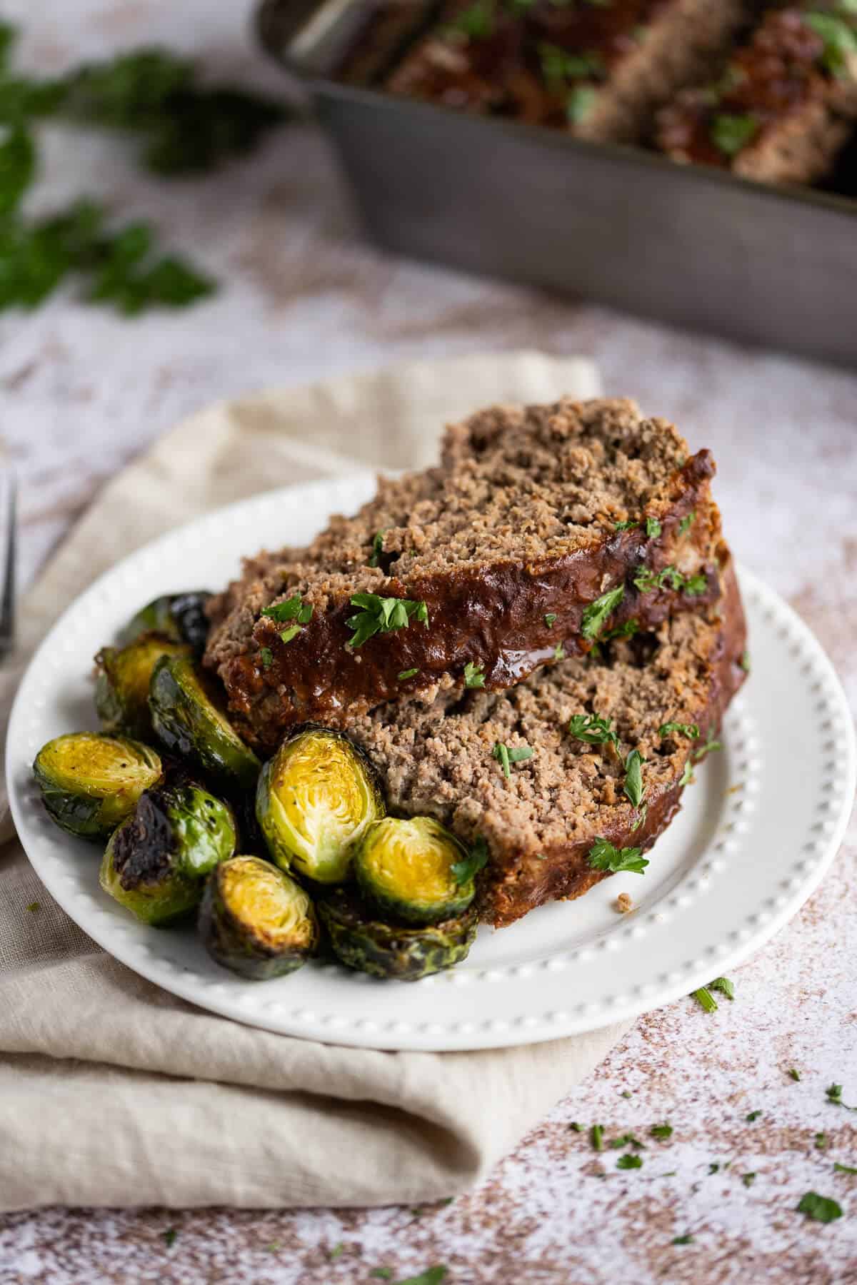 2 pieces of juicy meatloaf on a plate with roasted brussels sprouts