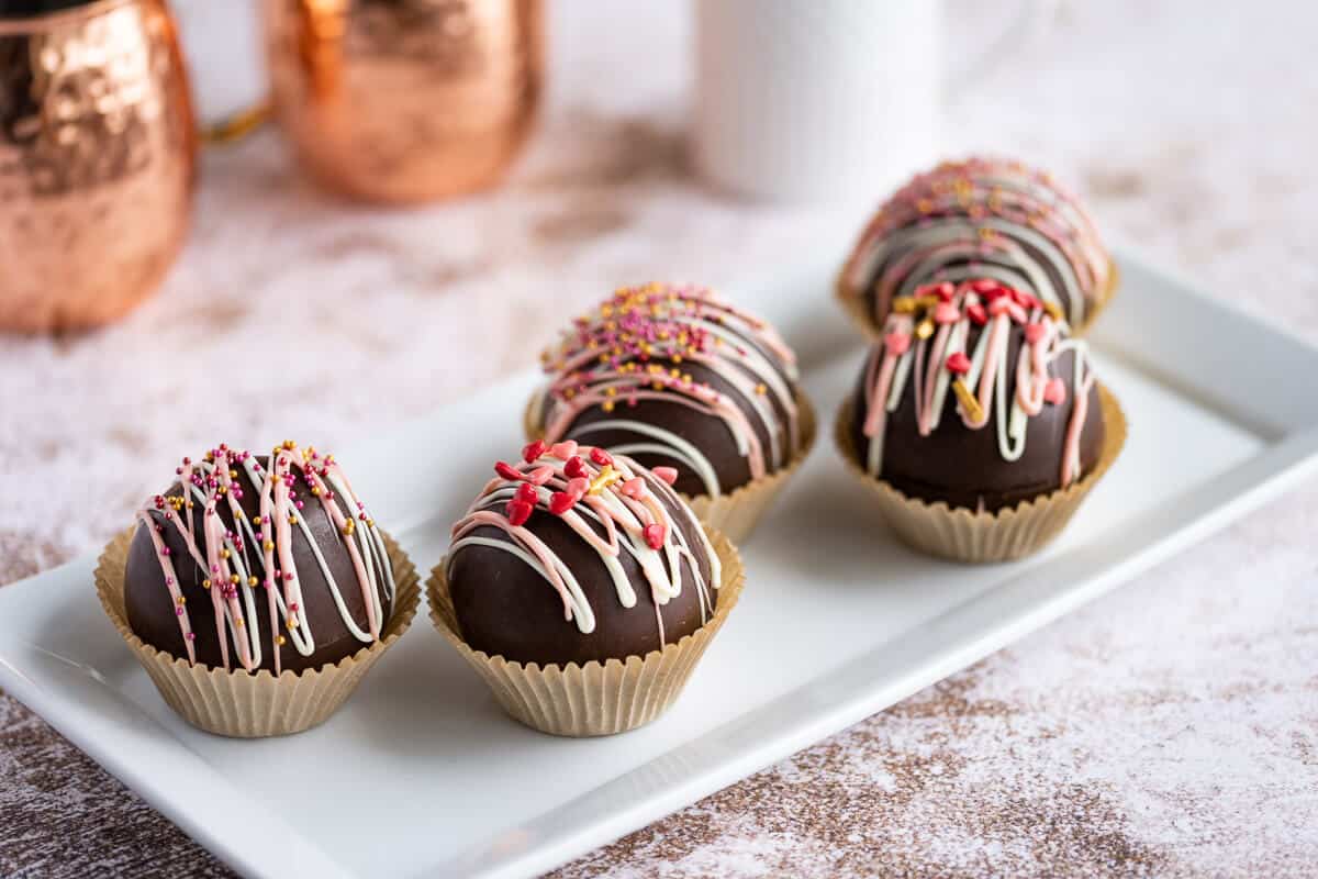 5 valentine themed hot cocoa bombs drizzled with white and pink chocolate and garnished with sprinkles