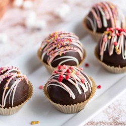 a platter of hot chocolate bombs decorated with pink and white chocolate drizzle and valentine sprinkles