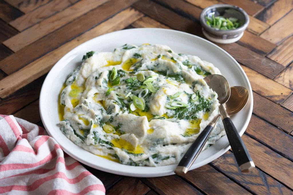 white serving bowl full of cauliflower mash colcannon with kale an olive oil