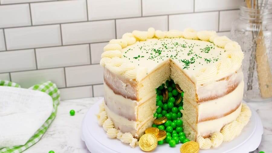 white layered cake with a slice missing and green candy and gold coin candy pouring out from the middle