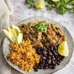 pork carnitas with rice and black beans, garnished with lime, avocado, and jalapenos