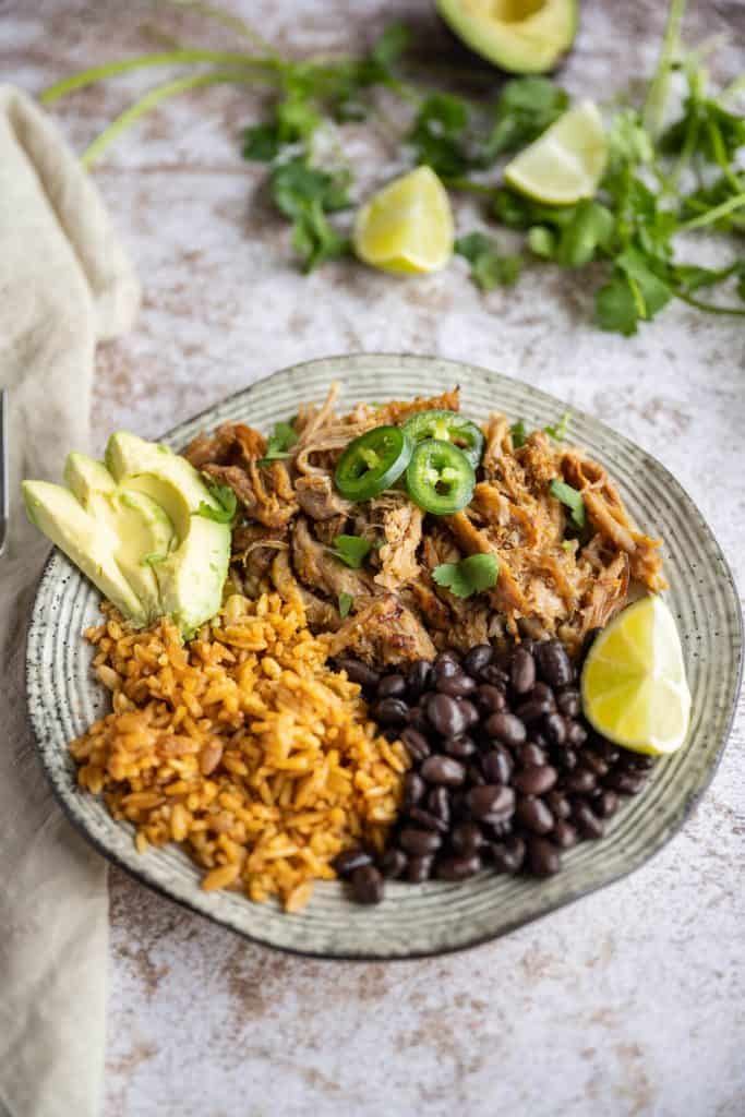pork carnitas with rice and black beans, garnished with lime, avocado, and jalapenos