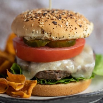 juicy burger topped with cheese, lettuce, tomato and the works on a seeded onion bun