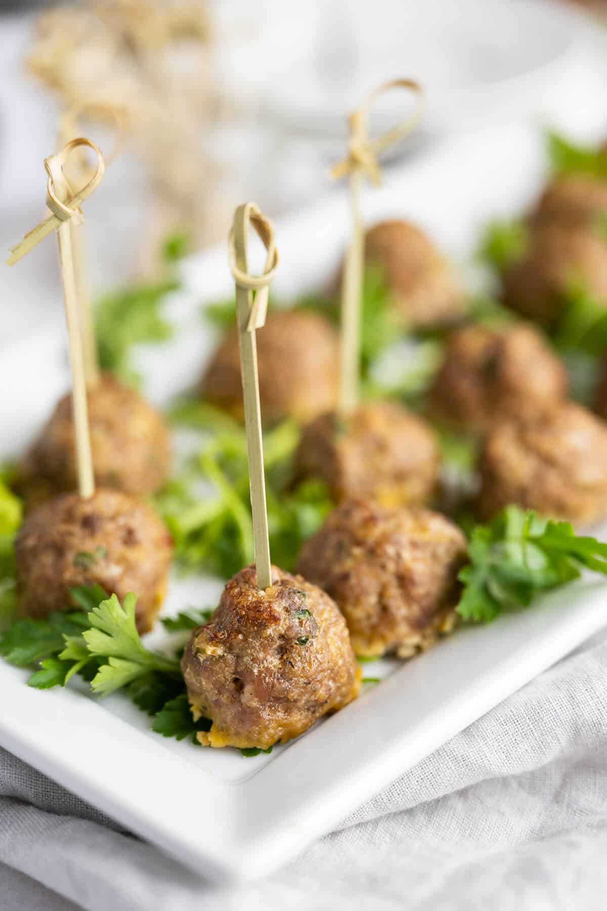 baked meatballs served as an appetizer with toothpicks on a white platter.