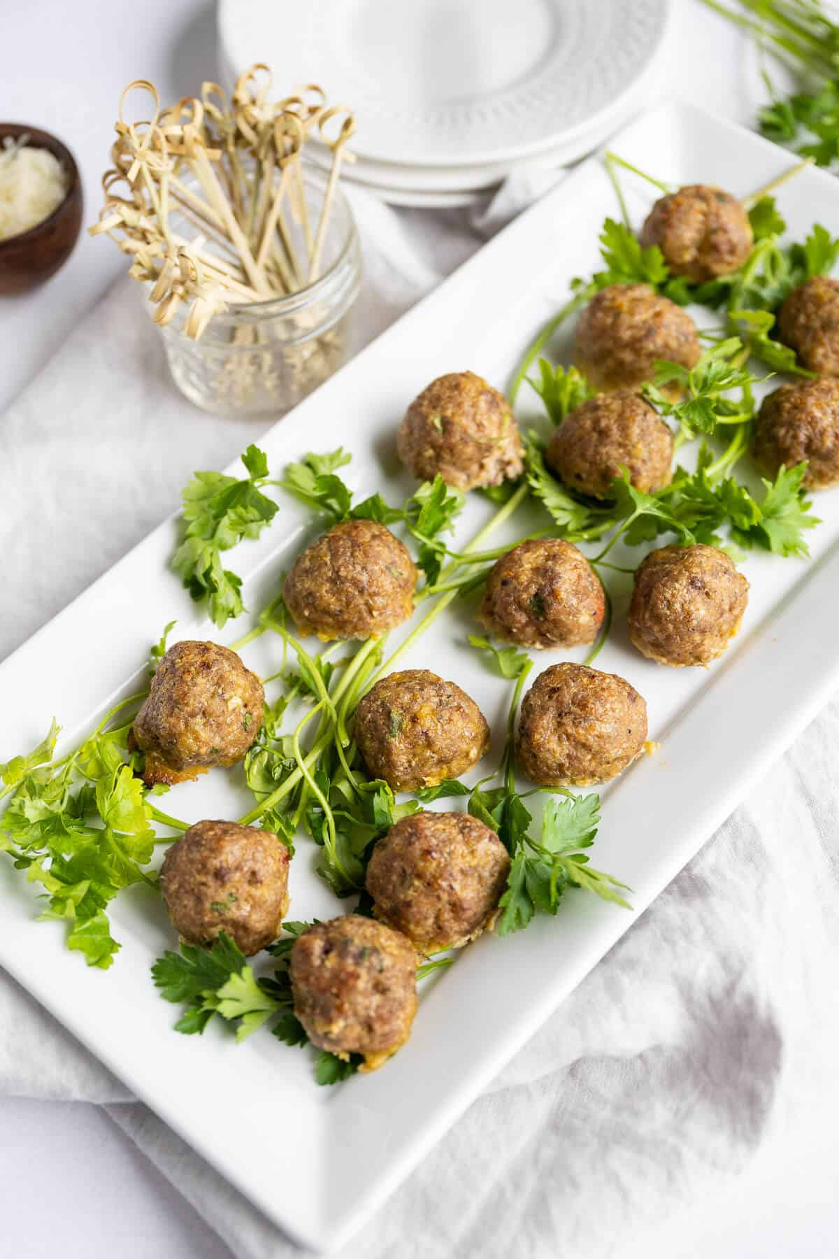 Oven baked seasoned meatballs without sauce on a platter garnished with fresh parsley.