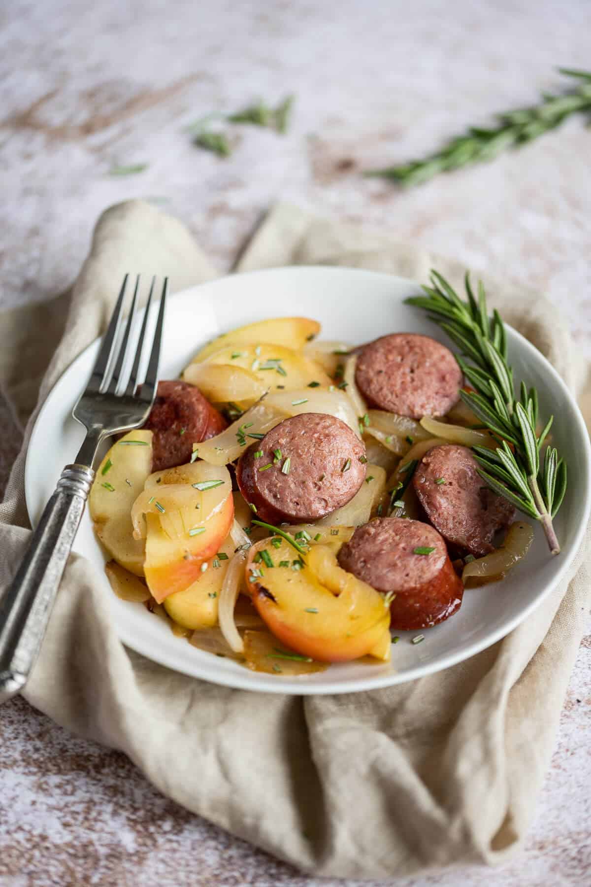 Smoked sausage with sliced apples and onions in a white bowl.