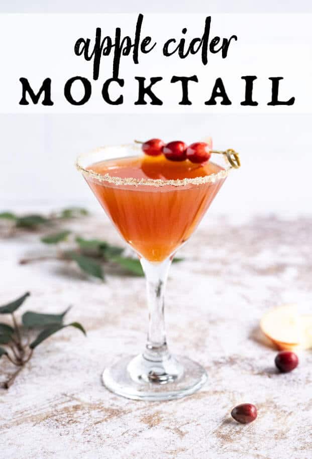 apple cider mocktail in a martini glass rimmed in sugar and garnished with fresh cranberries via @artfrommytable