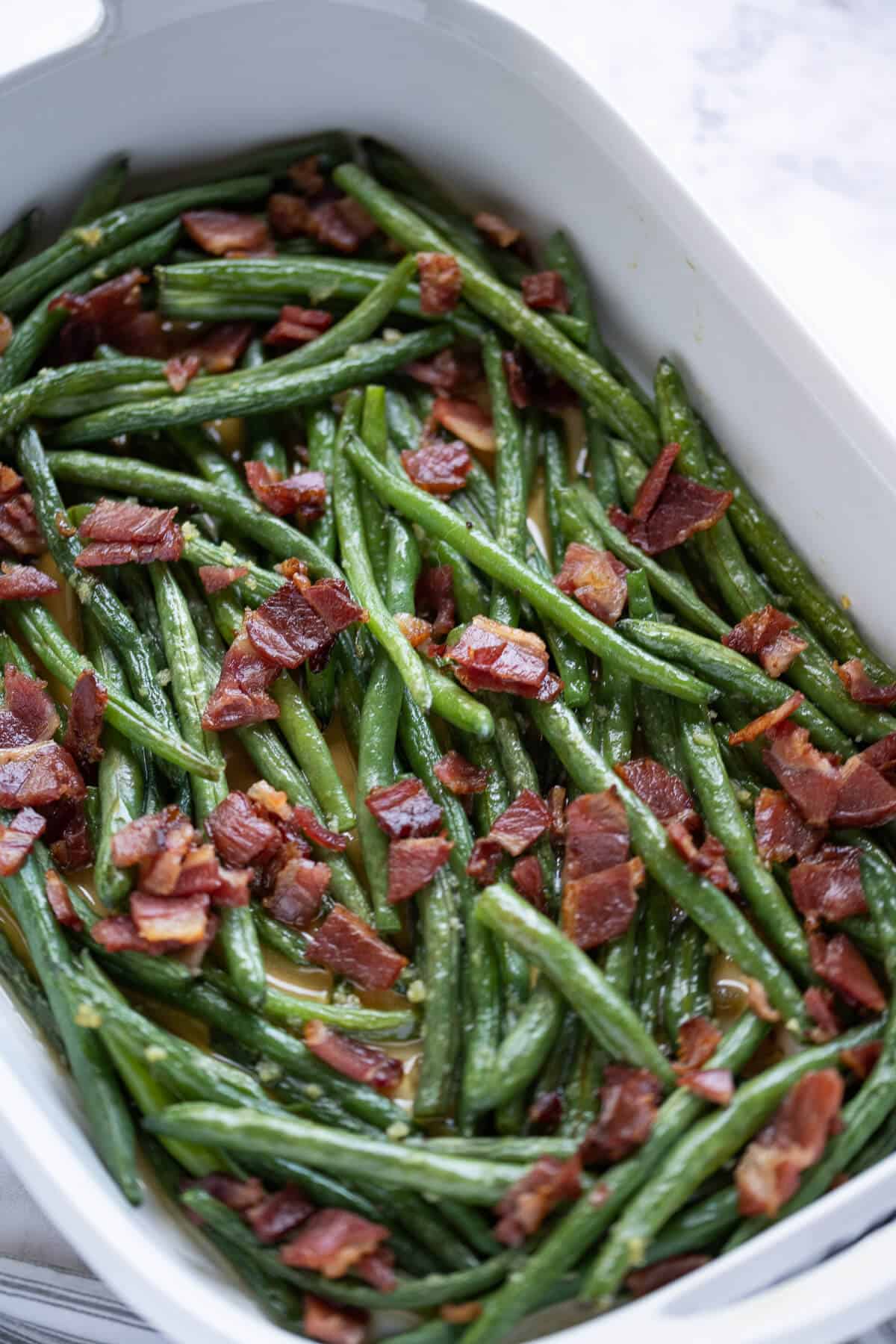 White casserole dish filled with green beans topped with bacon
