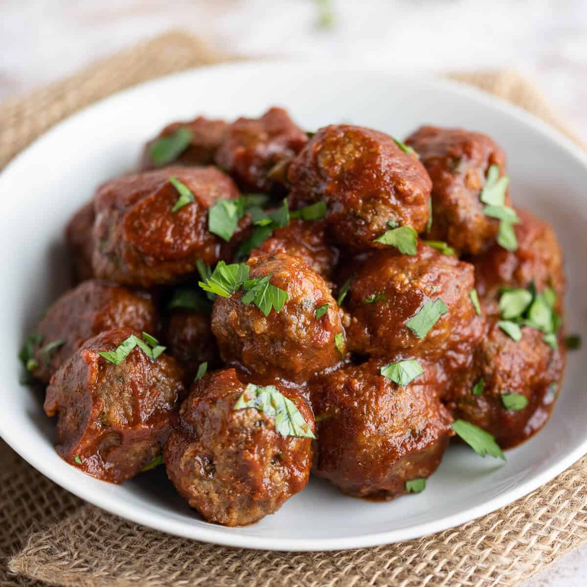 Small bbq meatballs in a white bowl garnished with parsley.