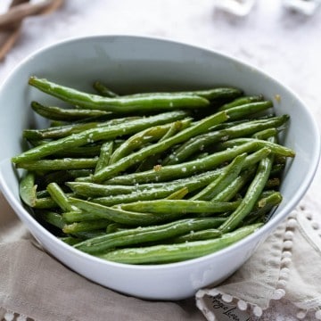 Roasted Green Beans glistening in garlic butter sauce in a white serving bowl.