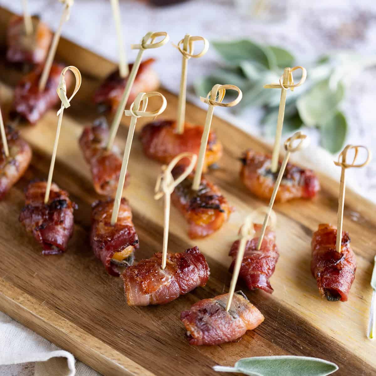 Bacon wrapped apricots brushed with maple syrup on a serving board with toothpicks.