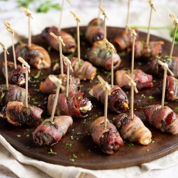Goat cheese stuffed dates, wrapped in bacon, on a round serving platter.