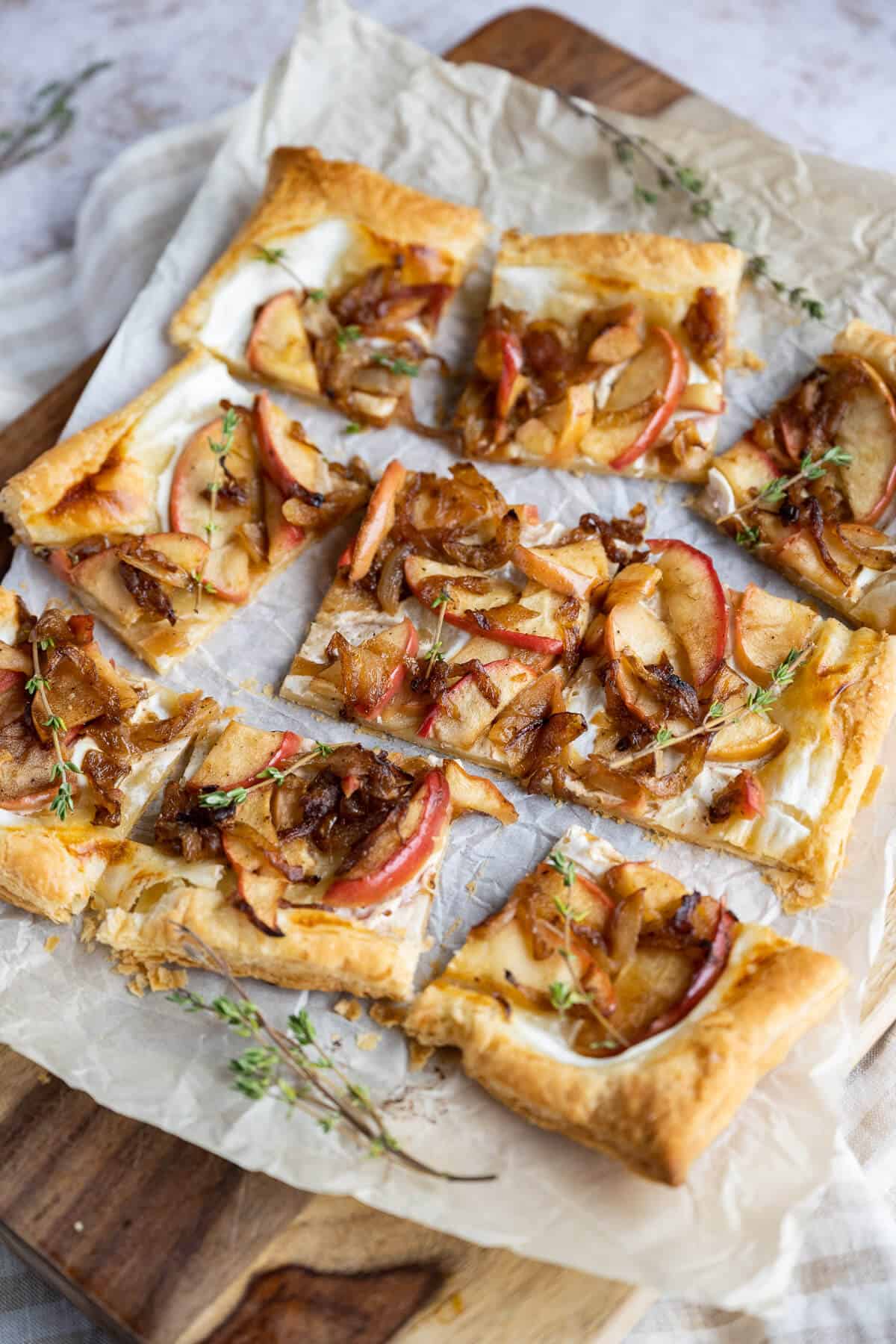 Onion tart on puff pastry cut into 9 squares on a cutting board garnished with fresh thyme.