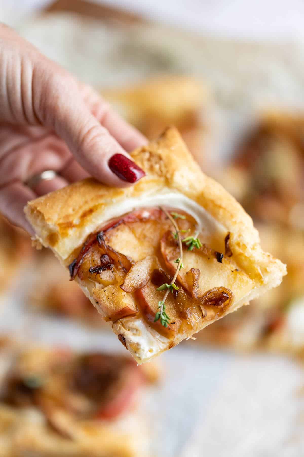 Hand picking up a slice of the Caramelized Onion Tart.