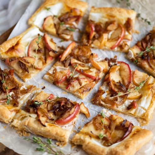 Onion tart on puff pastry cut into 9 squares on a cutting board garnished with fresh thyme.
