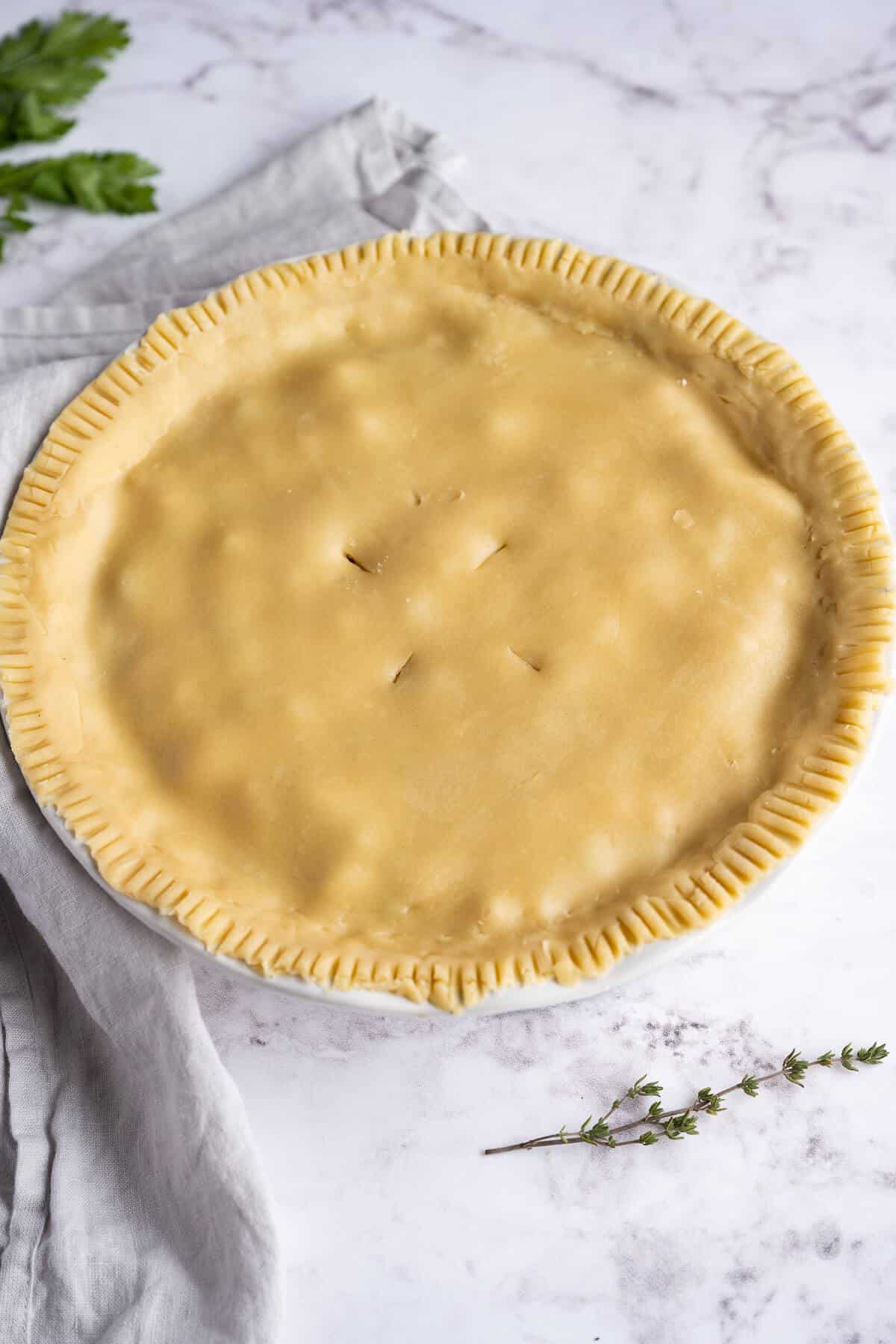 Turkey Pot pie before baking. Edges of crust are crimped and there are four slits in the center of the pie for venting.