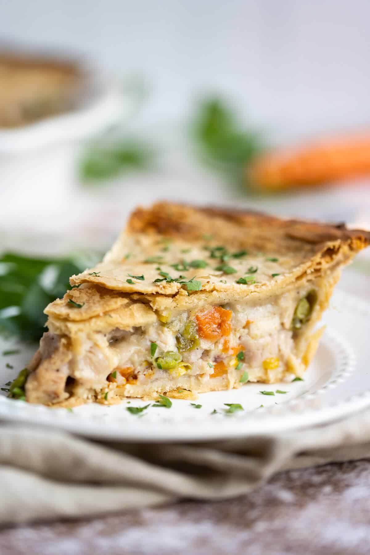 Slice of homemade turkey pot pie on a white plate garnished with fresh chopped parsley