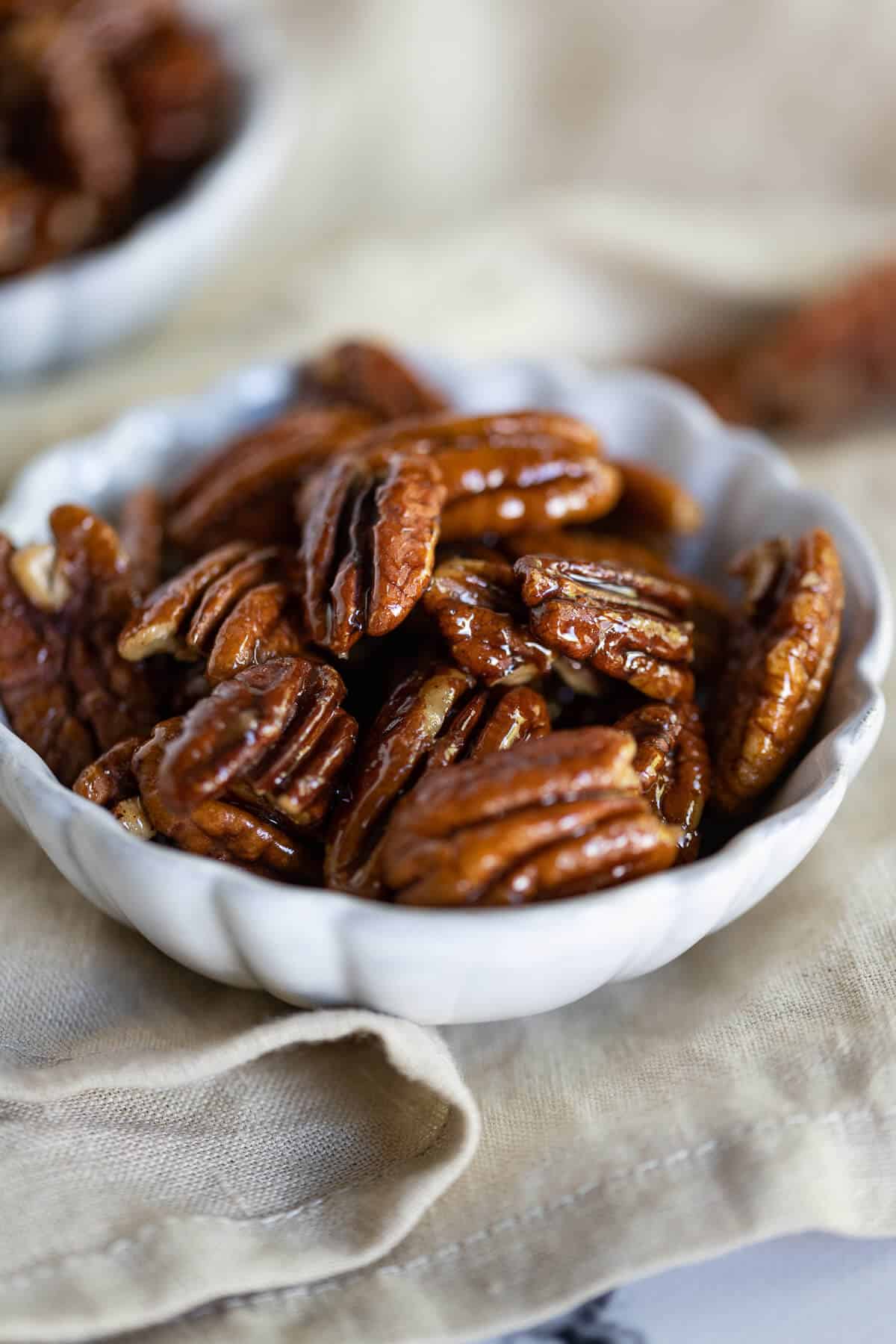 pecan halves that have been "candied" in brown sweetener, cinnamon and vanilla in a white bowl.