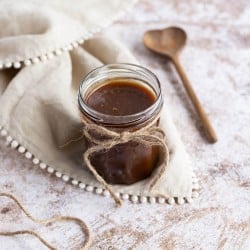 Salted Caramel sauce in an open jar with a heart-shaped wooden spoon alongside it.