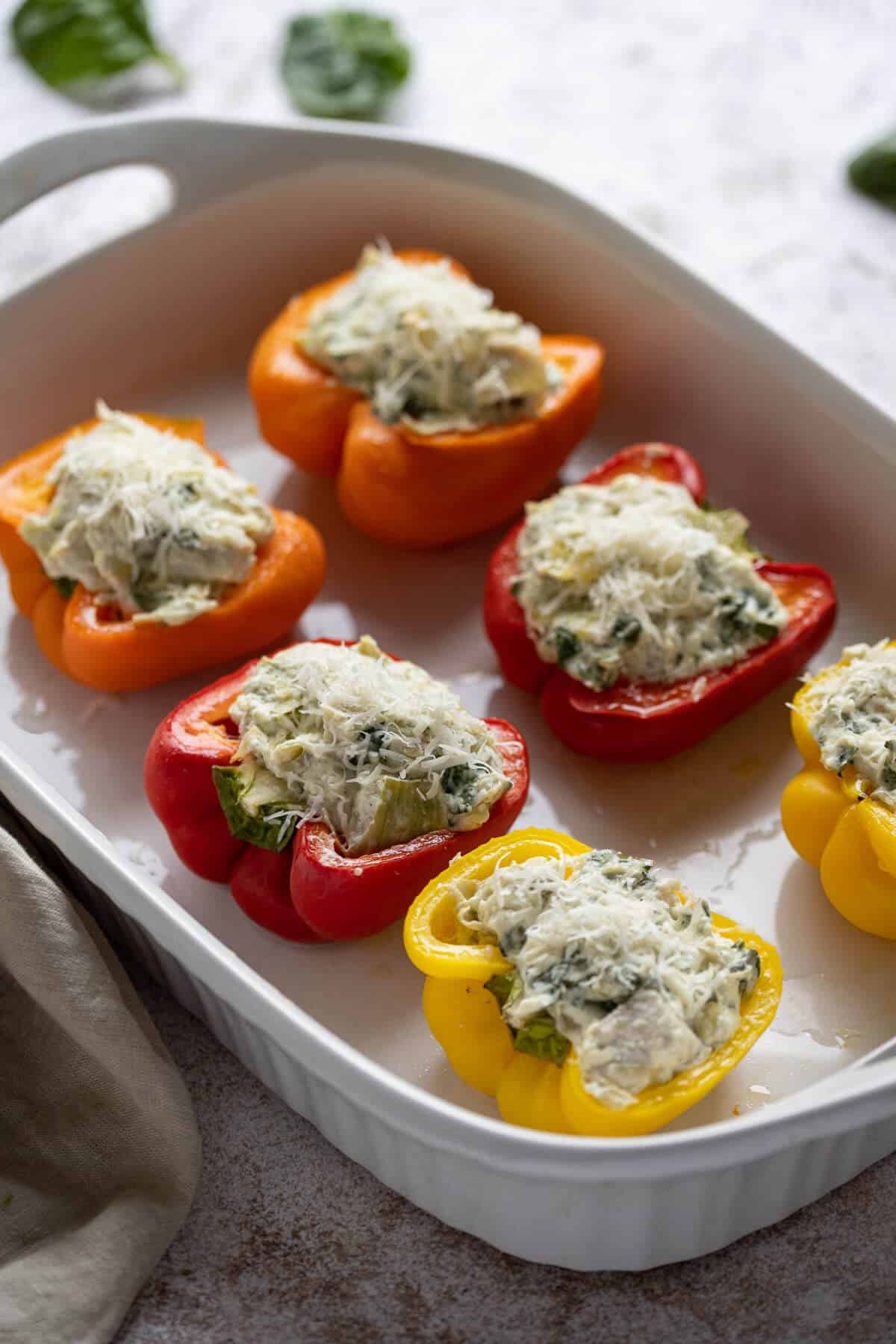 Bell peppers stuffed with chicken, spinach, and artichoke dip, in a white casserole dish.