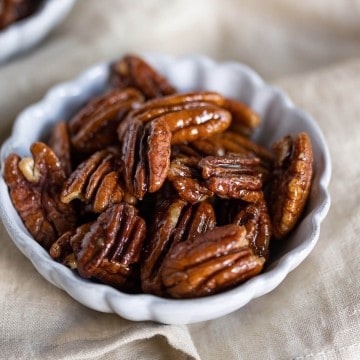 pecan halves that have been "candied" in brown sweetener, cinnamon and vanilla in a white bowl.