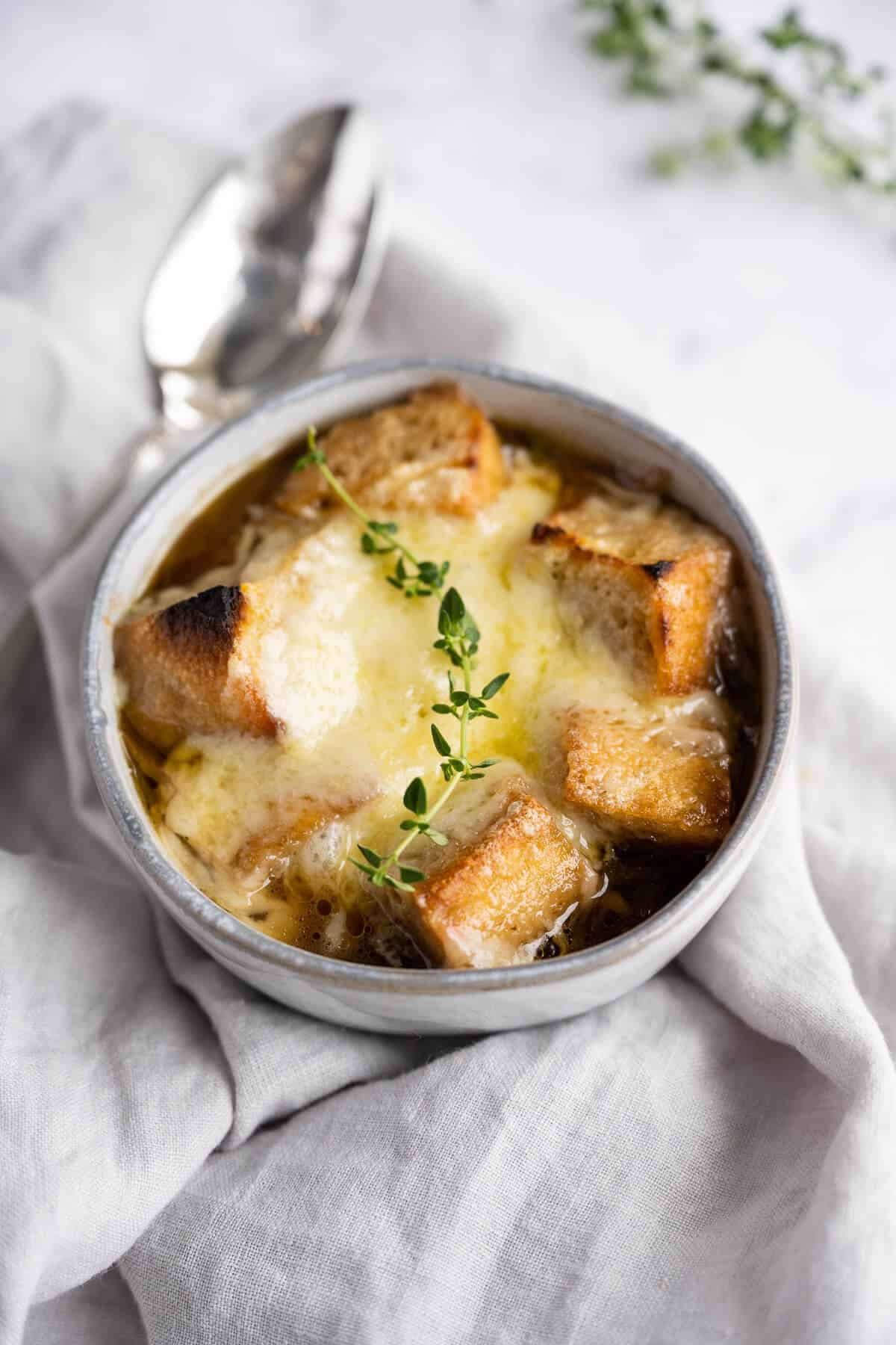 Bowl of French Onion Soup topped with crusty croutons and melted gruyere cheese, garnished with a sprig of thyme.