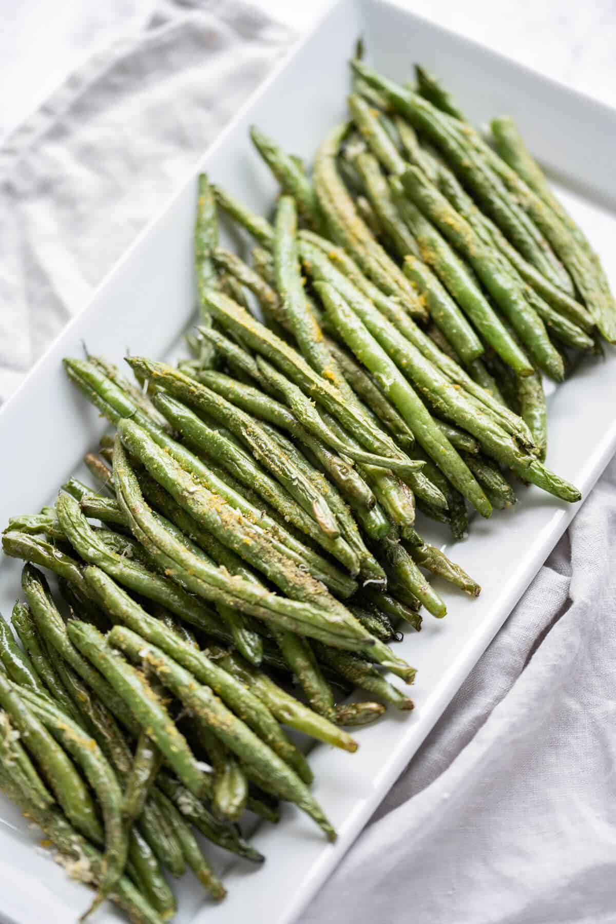 Air fried green beans with seasonings on a rectangle white platter.