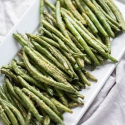 Air fried green beans with seasonings on a rectangle white platter.