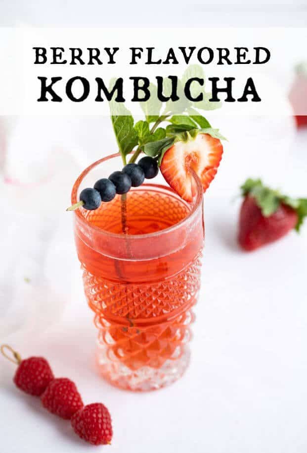 Berry flavored kombucha in a decorative tall glass garnished with a cocktail skewer of blueberries, a sliced strawberry, and a sprig of mint leaves. via @artfrommytable