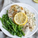 Chicken breast, cooked sous vide method, on a plate with green beans and rice. Chicken is garnished with a lemon slice.