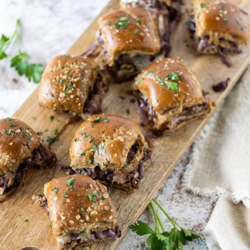 french dip sliders on a wooden serving board, garnished with fresh parsley