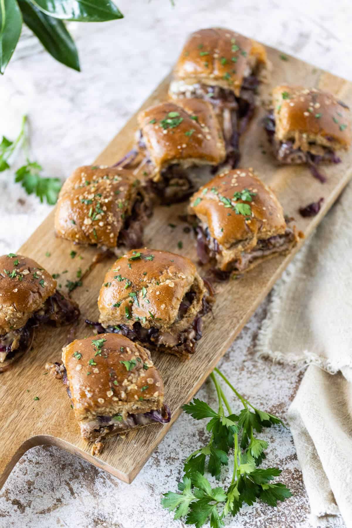 french dip sliders on a wooden serving board, garnished with fresh parsley